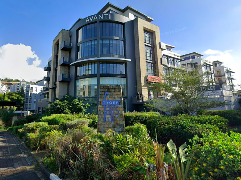 Modern multi-story office building featuring a prominent glass facade, stone cladding, and well-maintained landscaped grounds in a professional business park setting.