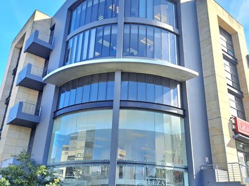 Modern multi-story office building facade featuring extensive glass curtain walling, prominent signage, and integrated balconies.