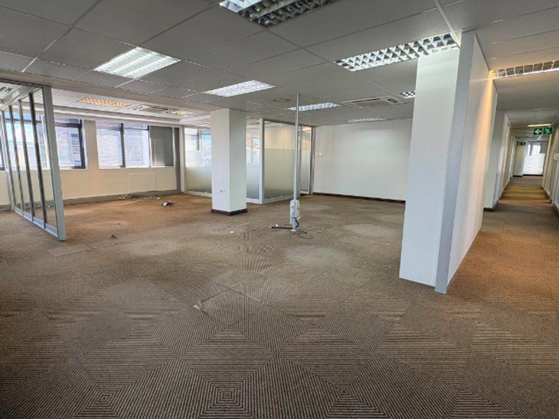 An open-plan office space featuring suspended ceilings, recessed lighting, glass partitions, and carpeted flooring, currently vacant and ready for refurbishment.