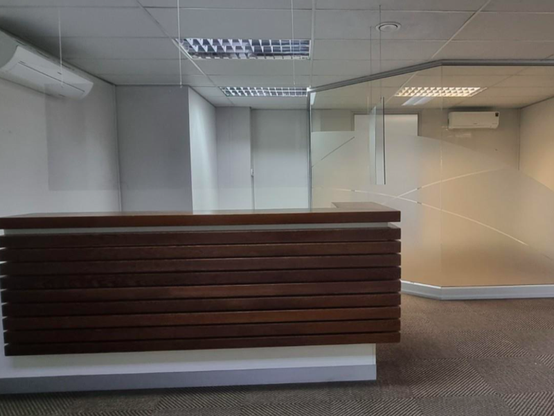 A professional office reception area featuring a built-in wooden desk, glass partitioning, suspended ceiling with recessed lighting, and split-system air conditioning.