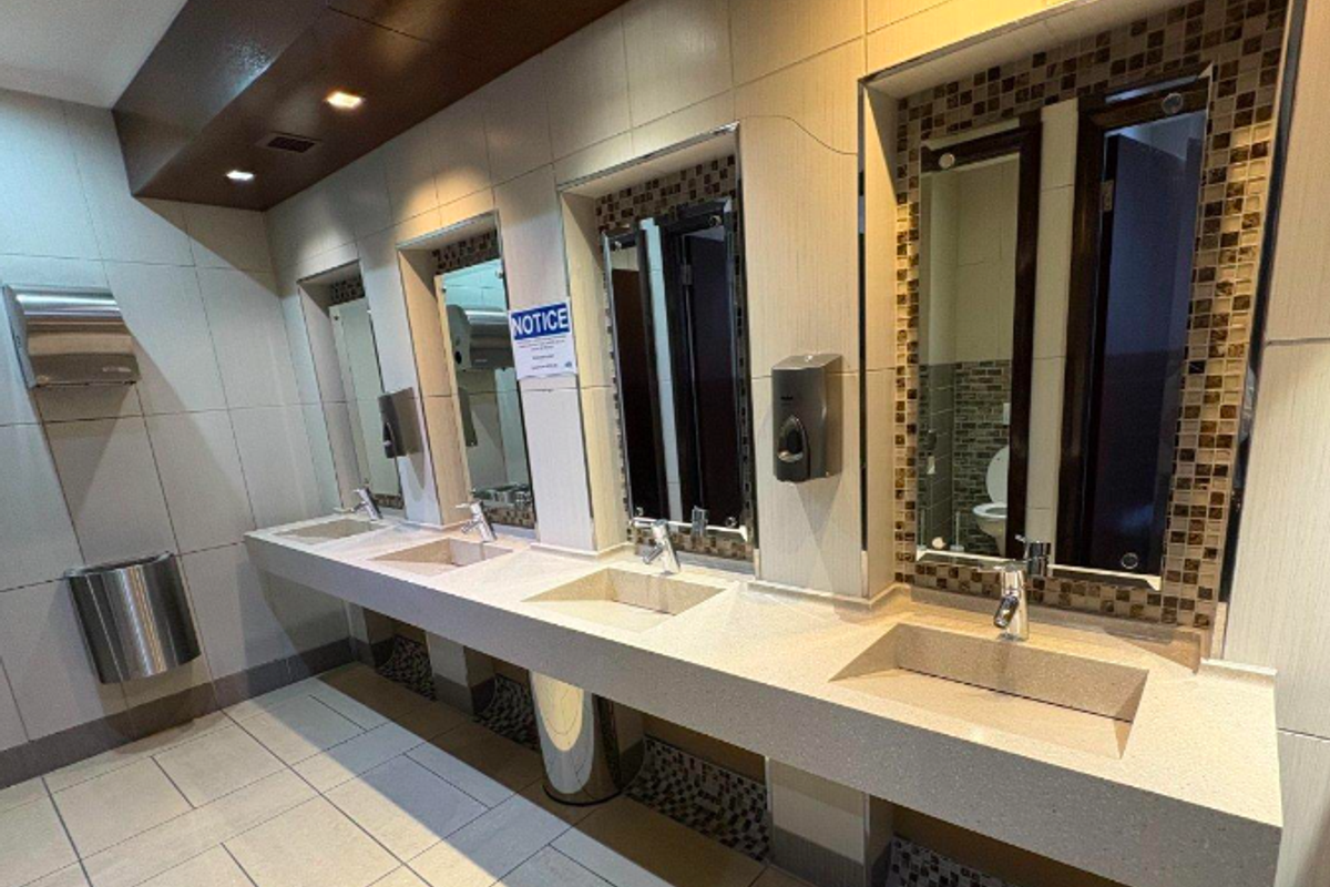 Modern office bathroom featuring a triple vanity with integrated stone sinks, chrome fixtures, mosaic tile accents, and recessed lighting.