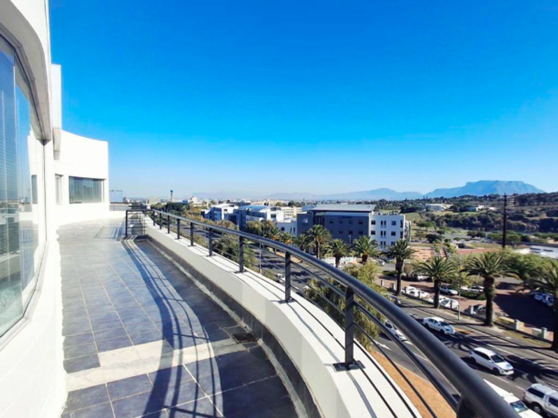 Spacious curved balcony featuring tiled flooring and a secure metal balustrade, offering expansive views of the surrounding urban landscape.