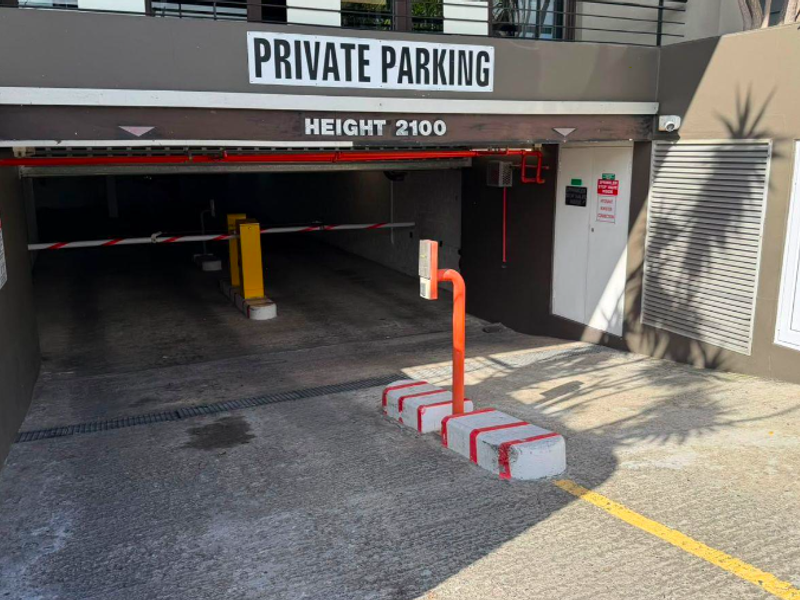Secure private parking entrance featuring an automated boom gate, access control system, and clear height clearance signage.