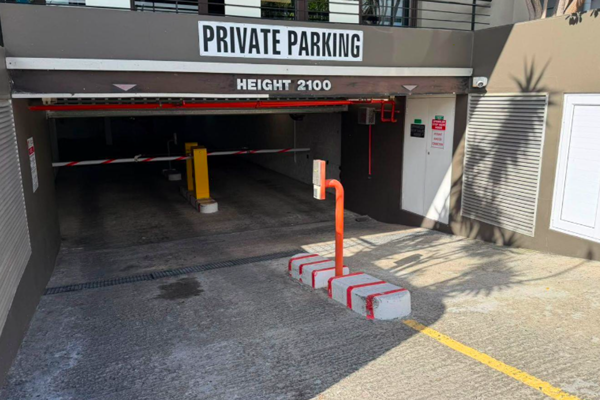 Secure private parking entrance featuring an automated boom gate, access control system, and clear height clearance signage.