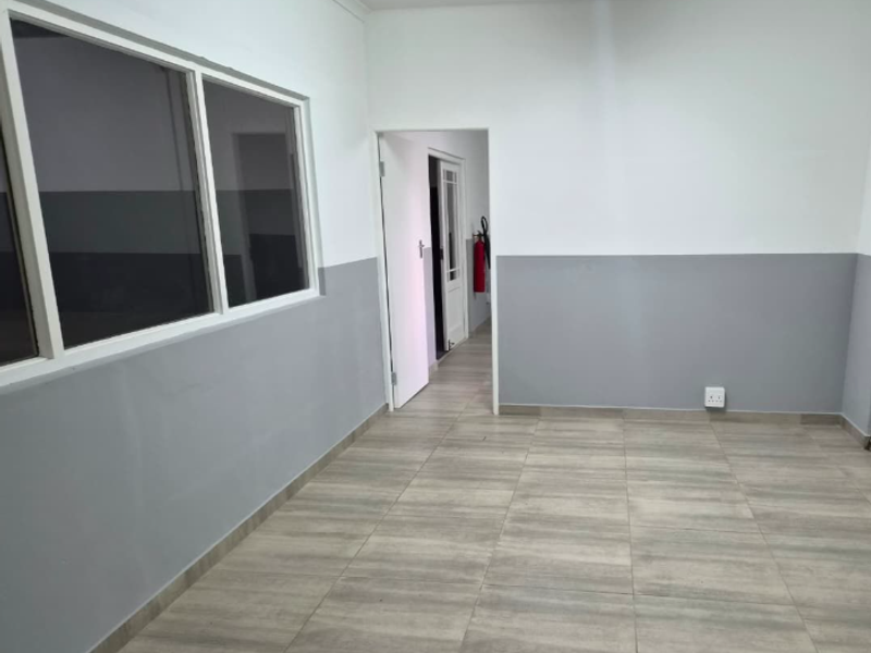 A clean, vacant office space featuring neutral grey and white walls, modern tiled flooring, and large windows providing natural light.