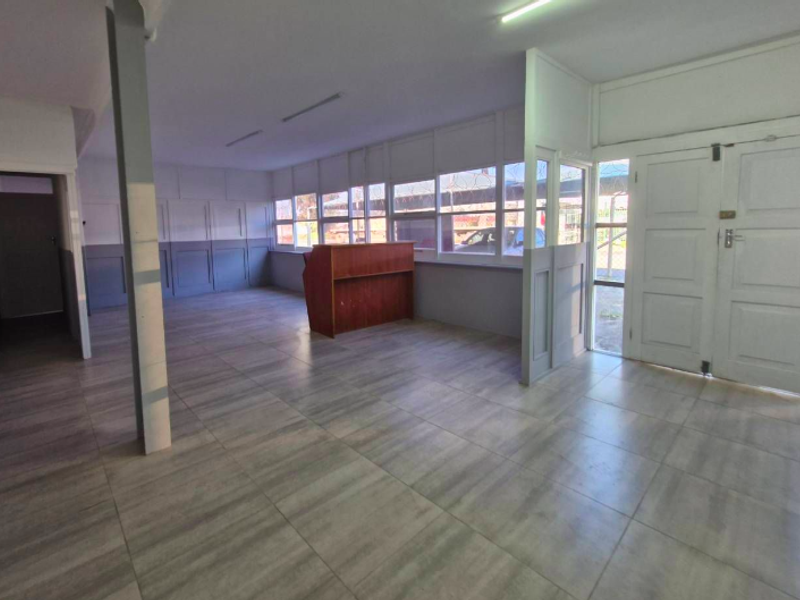 Spacious open-plan industrial office area featuring tiled flooring, panelled walls, and large windows with security bars, providing a bright and functional workspace.