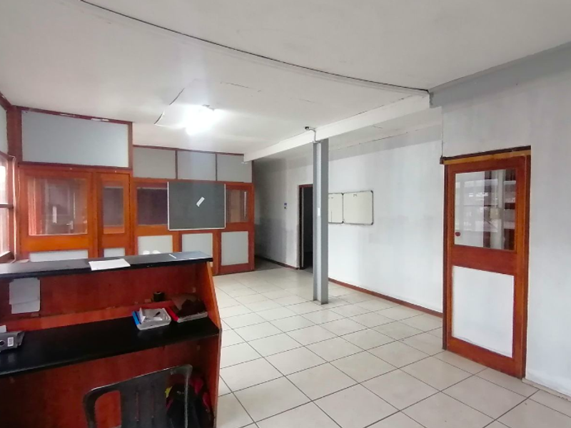 An open-plan office space featuring tiled flooring, timber-framed glass partitions, and a built-in reception counter, requiring some ceiling maintenance.