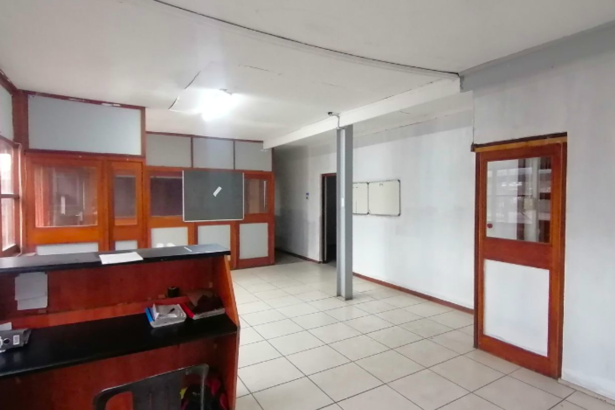 An open-plan office space featuring tiled flooring, timber-framed glass partitions, and a built-in reception counter, requiring some ceiling maintenance.