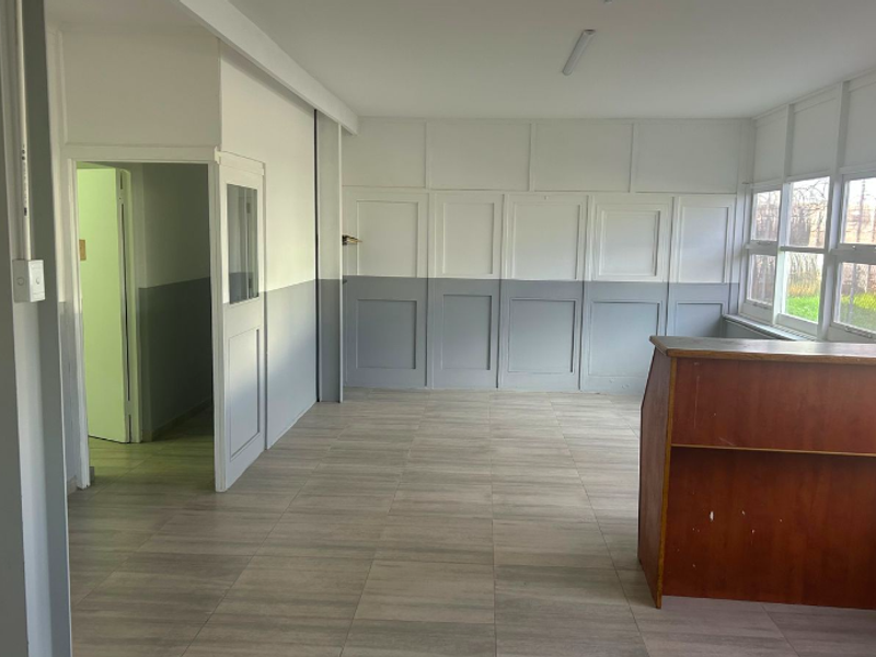 A bright, open-plan office space featuring neutral wainscoting, tiled flooring, and large windows providing natural light.