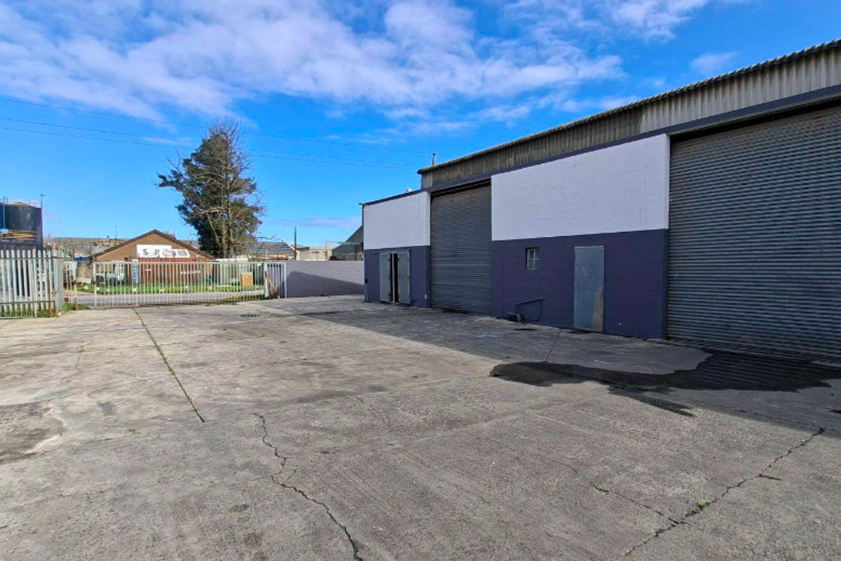 Industrial property exterior featuring a large concrete yard, secure metal fencing, and multiple roller shutter doors for vehicle or goods access.