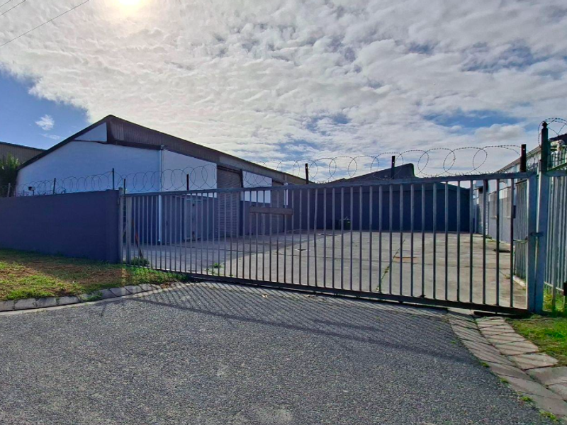 Industrial property exterior featuring a secure gated entrance, concrete driveway, and perimeter wall with razor wire fencing.