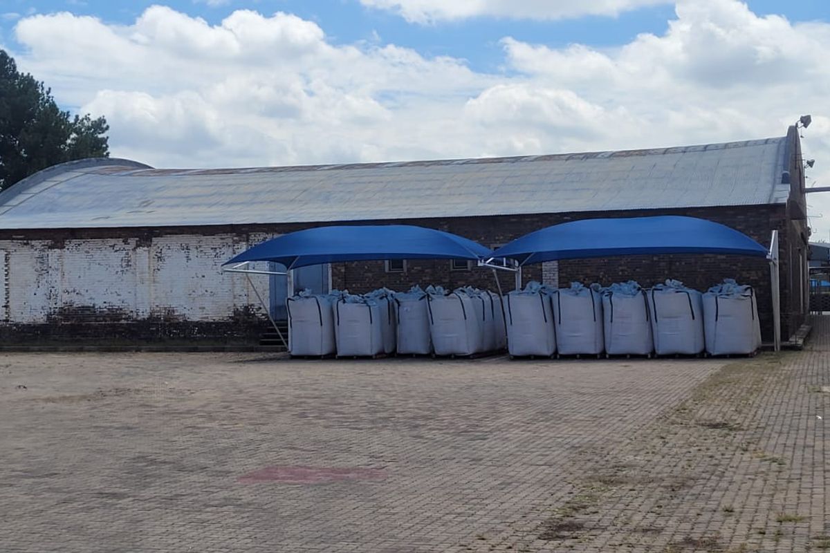 Exterior view of an industrial warehouse facility featuring a curved roof, brick facade, and a paved yard area with shade-covered storage.