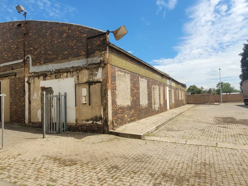 Exterior view of an industrial warehouse building featuring brick construction, paved yard area, and security fencing.