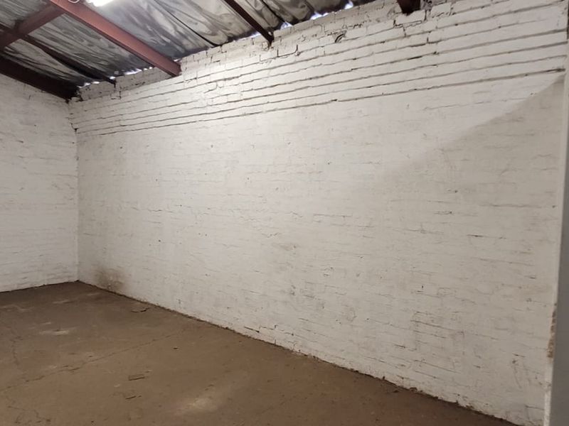 An empty industrial utility space featuring exposed steel roof beams, painted brick masonry walls, and a concrete floor, suitable for storage or workshop use.