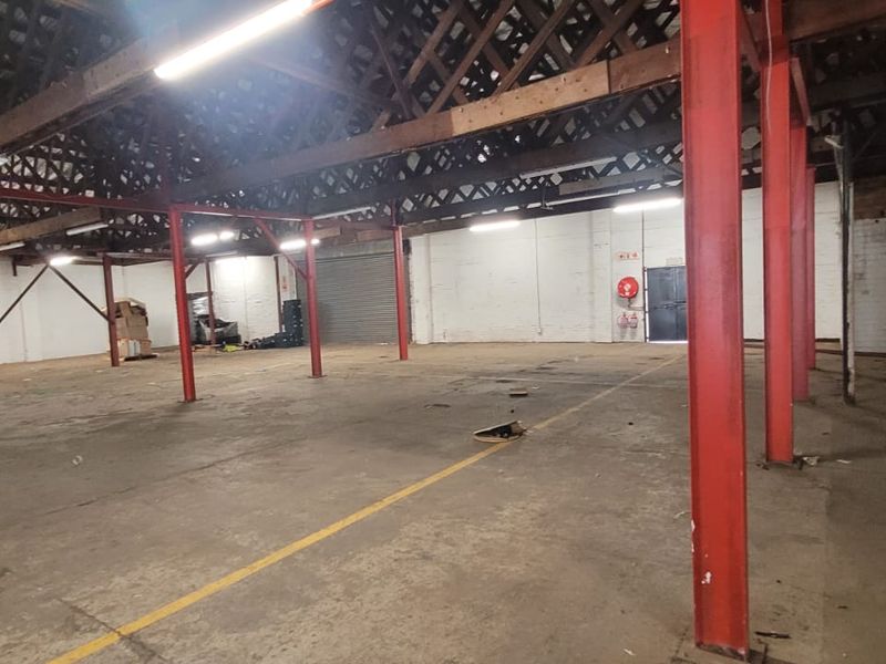 Spacious industrial warehouse featuring high ceilings with exposed timber trusses, red steel support columns, and durable concrete flooring throughout.
