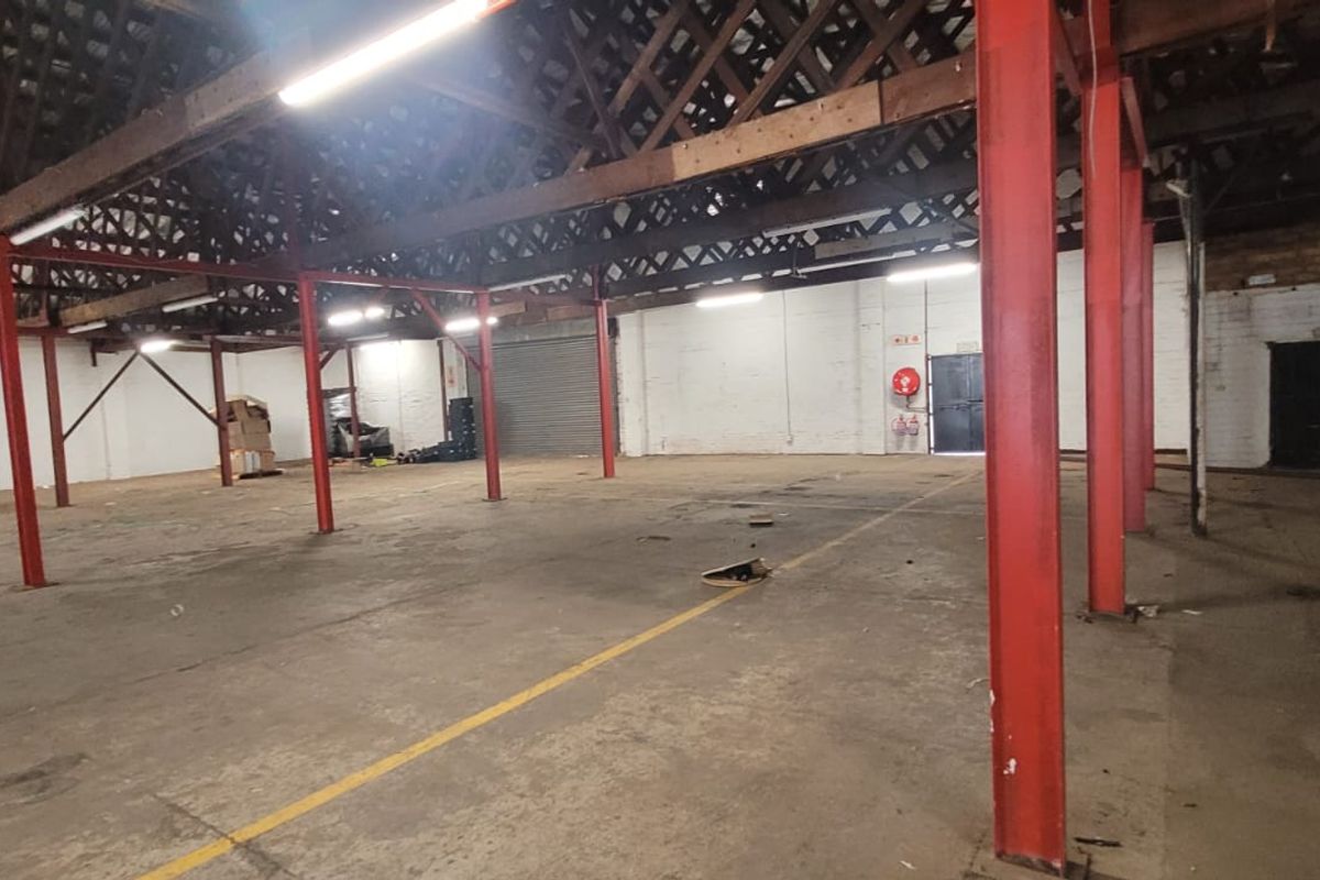Spacious industrial warehouse featuring high ceilings with exposed timber trusses, red steel support columns, and durable concrete flooring throughout.