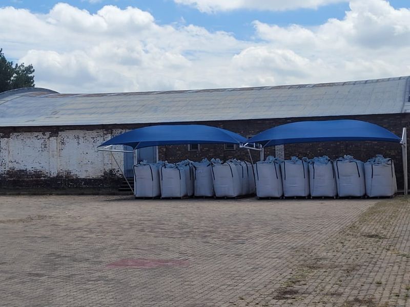 Exterior view of an industrial warehouse facility featuring a curved roof, brick facade, and a paved yard area with shade-covered storage.