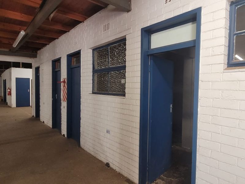 Industrial warehouse interior featuring exposed timber ceiling beams, painted brick walls, and multiple access doors leading to partitioned utility or office spaces.