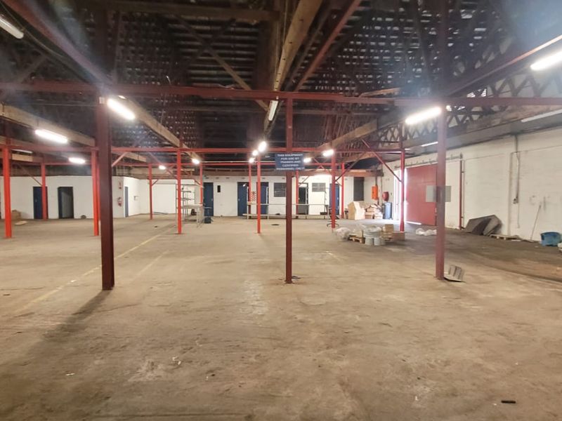 Expansive industrial warehouse space featuring high ceilings, exposed steel support beams, concrete flooring, and multiple access points.
