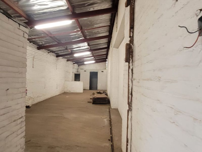 An industrial warehouse space featuring exposed brick walls, a metal roof structure, and concrete flooring, suitable for storage or workshop use.