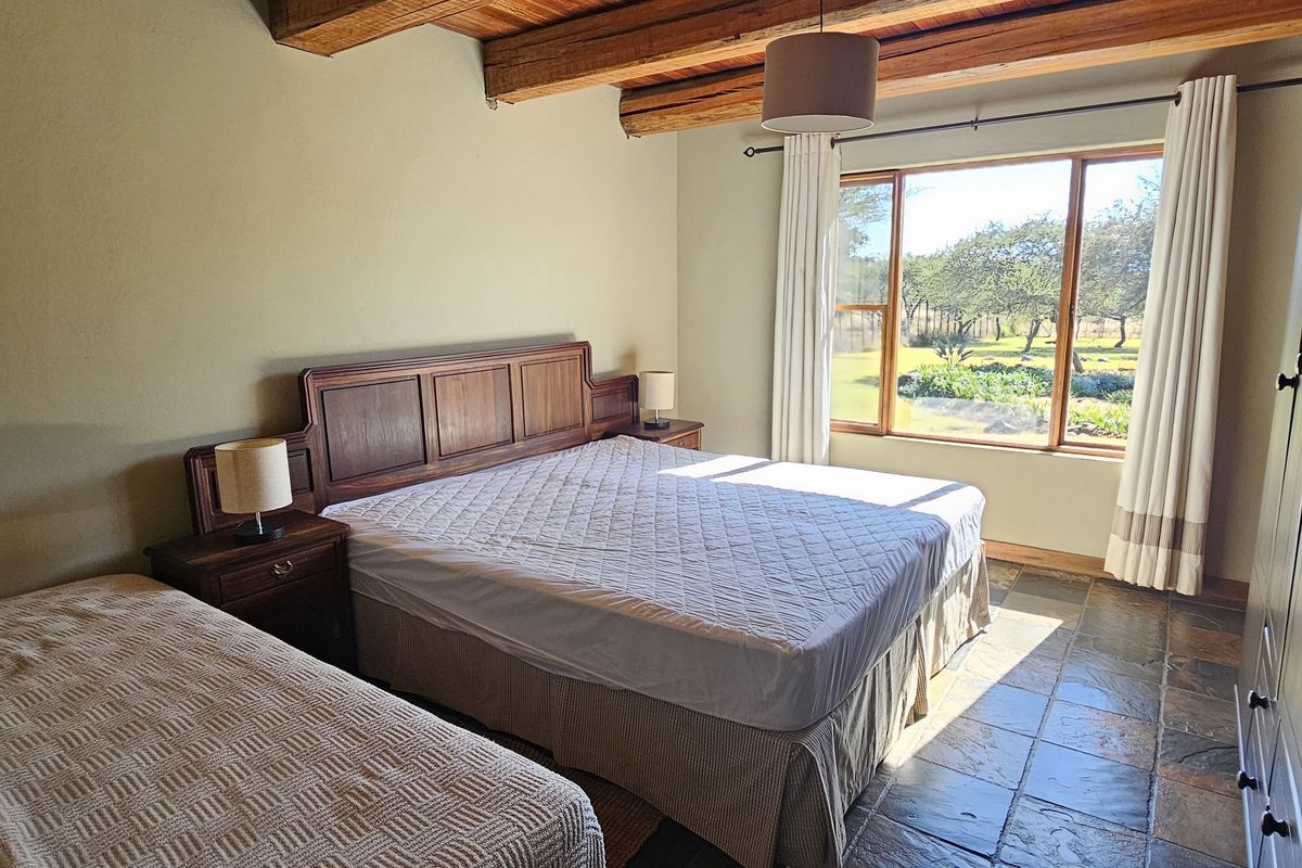 Spacious bedroom featuring rustic exposed timber ceiling beams, durable slate tile flooring, and a large window offering pleasant views of the surrounding farm garden.