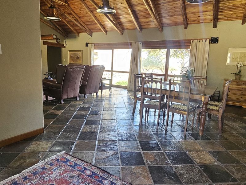 Spacious open-plan living and dining area featuring rustic slate tile flooring and a high exposed timber beam ceiling with large glass doors.