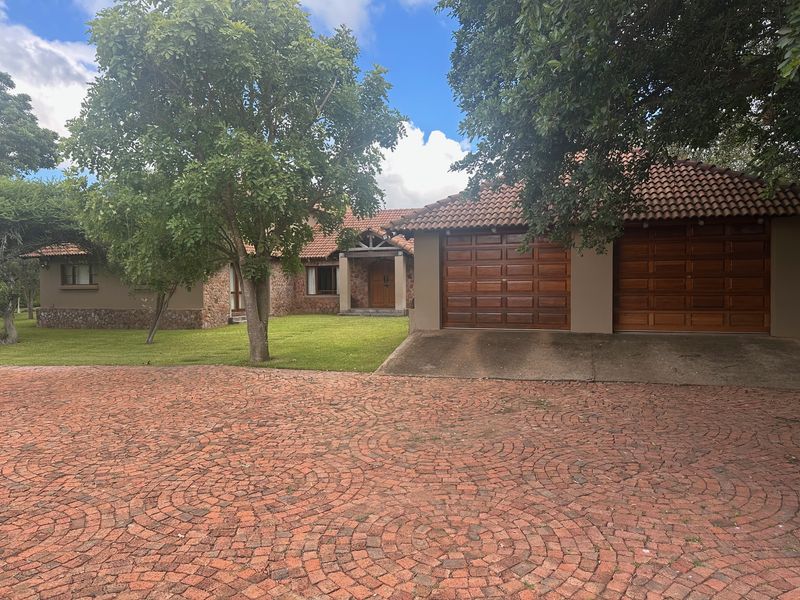 Front view of a farm-style residence featuring stone cladding, a tiled roof, and a spacious double garage with a circular brick-paved driveway.