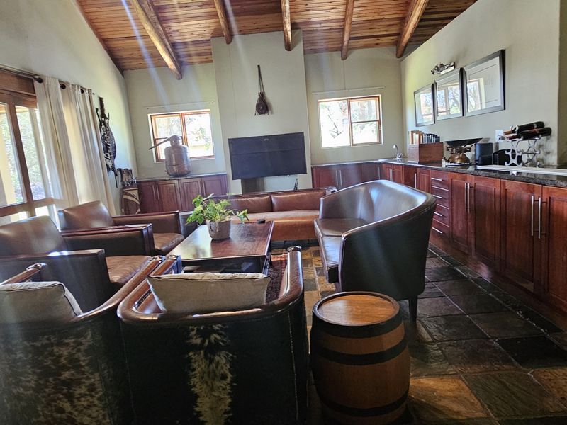 Spacious open-plan living and kitchen area featuring exposed timber beam ceilings, stone tile flooring, and extensive built-in cabinetry with granite countertops.