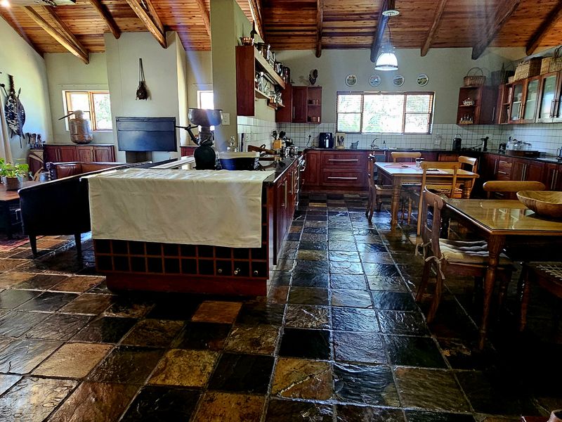 Spacious open-plan living and kitchen area featuring rustic exposed timber beam ceilings, slate tile flooring, and a central kitchen island with built-in cabinetry.