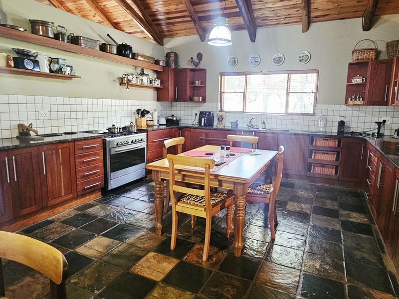 Spacious farmhouse kitchen featuring warm wooden cabinetry, granite countertops, slate flooring, and exposed timber ceiling beams, creating a rustic and functional culinary space.