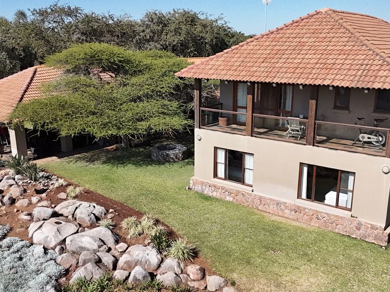 Aerial view of a two-story farm residence featuring terracotta roofing, stone cladding, and a spacious upper-level balcony overlooking a landscaped garden.