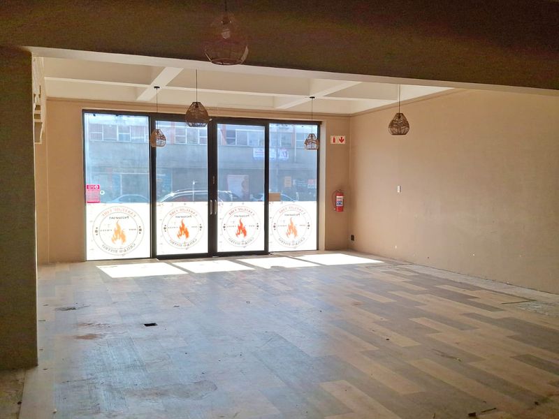 Spacious open-plan retail unit featuring large glass storefront windows, recessed ceiling beams, and vinyl plank flooring, ready for custom fit-out.