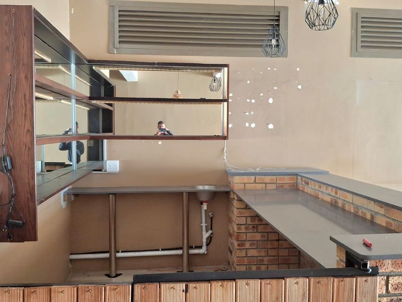 A vacant retail bar area featuring a brick-based counter, stone top, integrated sink, and wall-mounted shelving with mirrored accents, requiring cosmetic updates.
