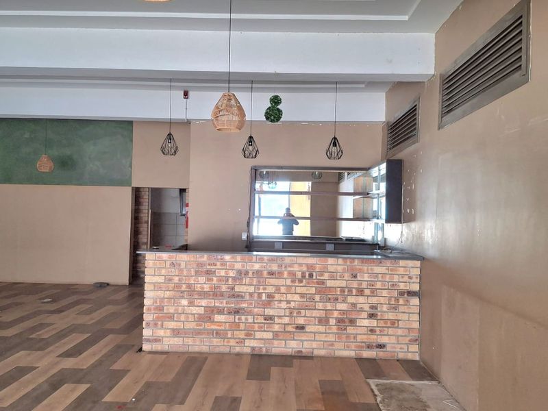 Open-plan retail space featuring a brick service counter, modern pendant lighting, HVAC ventilation, and durable laminate flooring, suitable for various commercial business applications.
