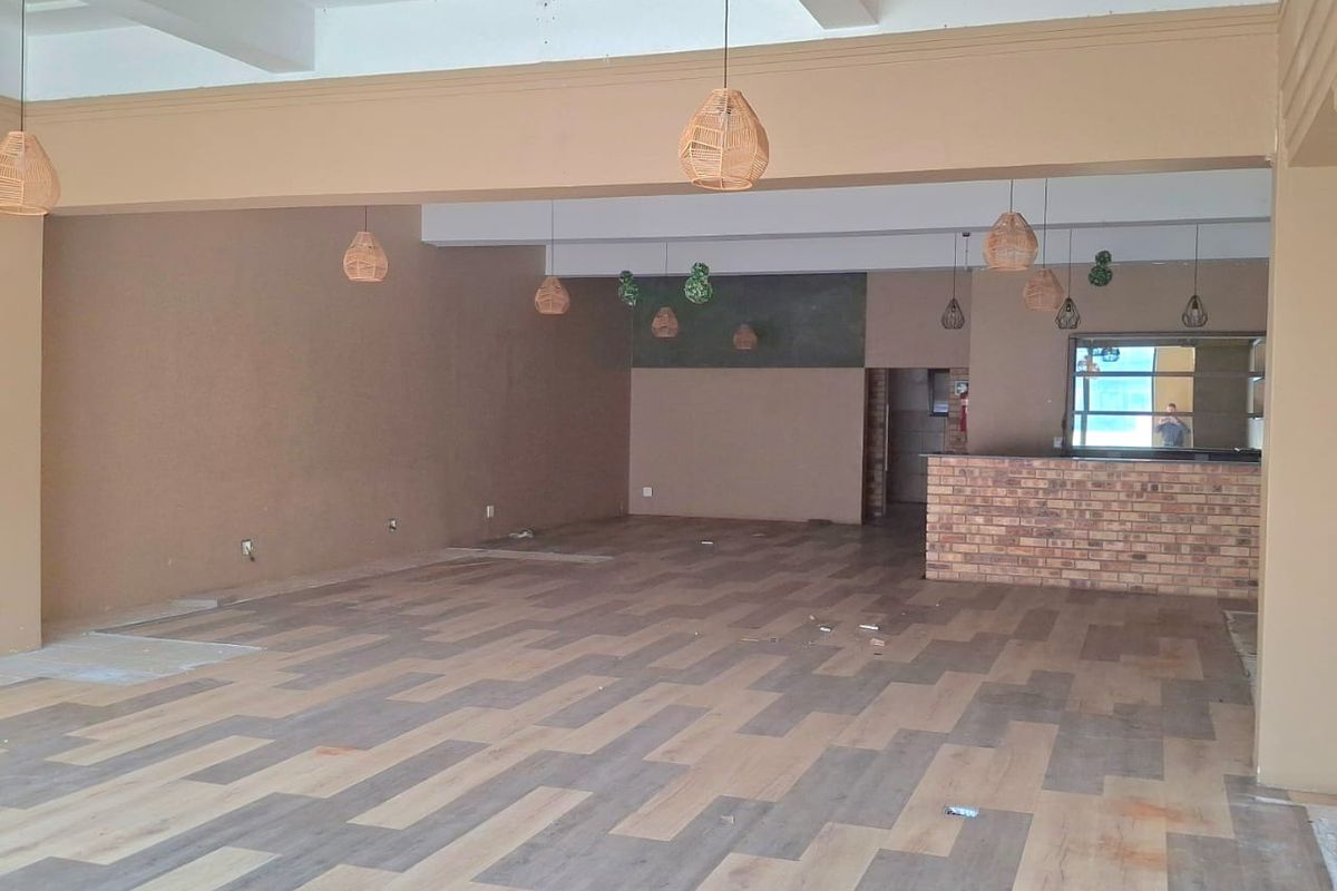 Spacious open-plan retail area featuring laminate flooring, a brick service counter, and exposed beam ceilings with pendant lighting.