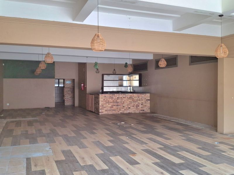 Spacious open-plan retail or hospitality area featuring a brick-faced service counter, exposed beam ceiling, and modern laminate flooring throughout.