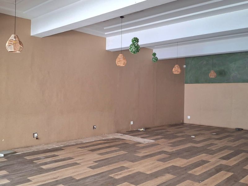 Spacious open-plan retail area featuring exposed beam ceilings, modern laminate flooring, and decorative pendant lighting, ready for custom fit-out.