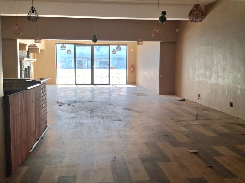 Spacious open-plan retail area featuring a built-in service counter, large glass sliding doors for natural light, and pendant lighting throughout.