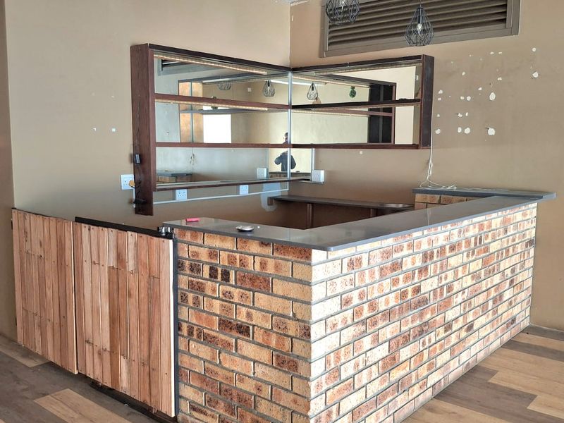 A vacant retail bar area featuring a brick counter, wooden accents, built-in mirror shelving, and pendant lighting, ready for custom fit-out.