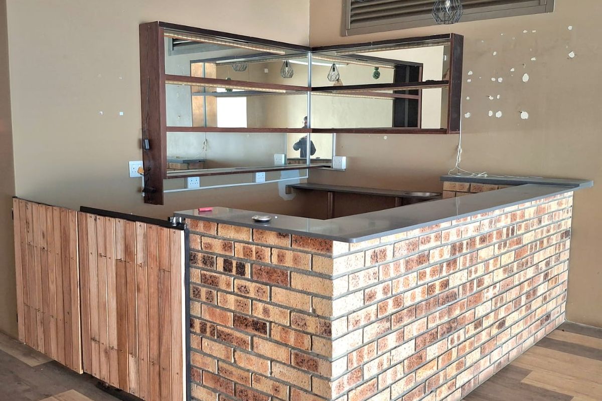 A vacant retail bar area featuring a brick counter, wooden accents, built-in mirror shelving, and pendant lighting, ready for custom fit-out.