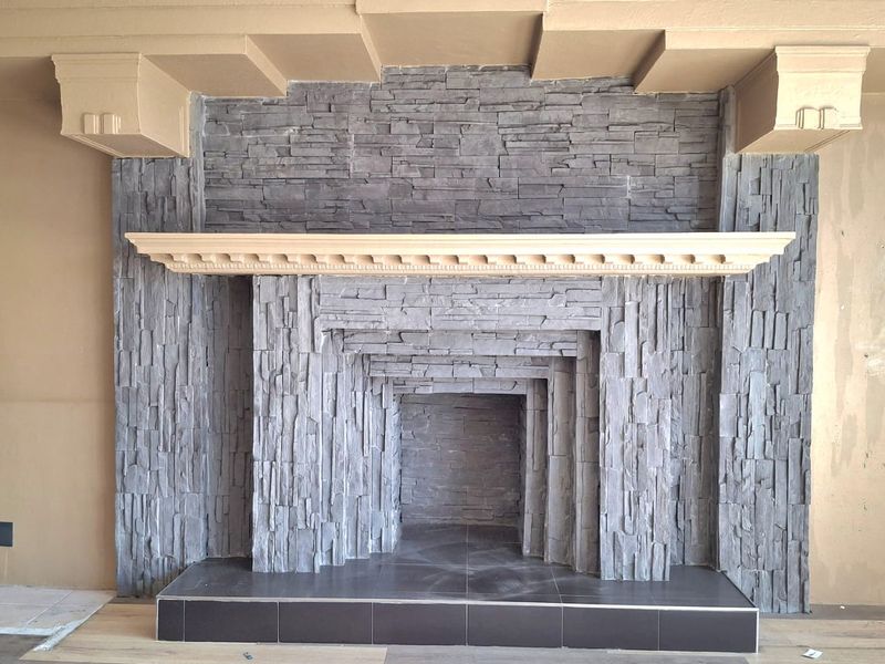 A spacious living area featuring a prominent stone fireplace with a decorative wooden mantelpiece and modern laminate flooring.