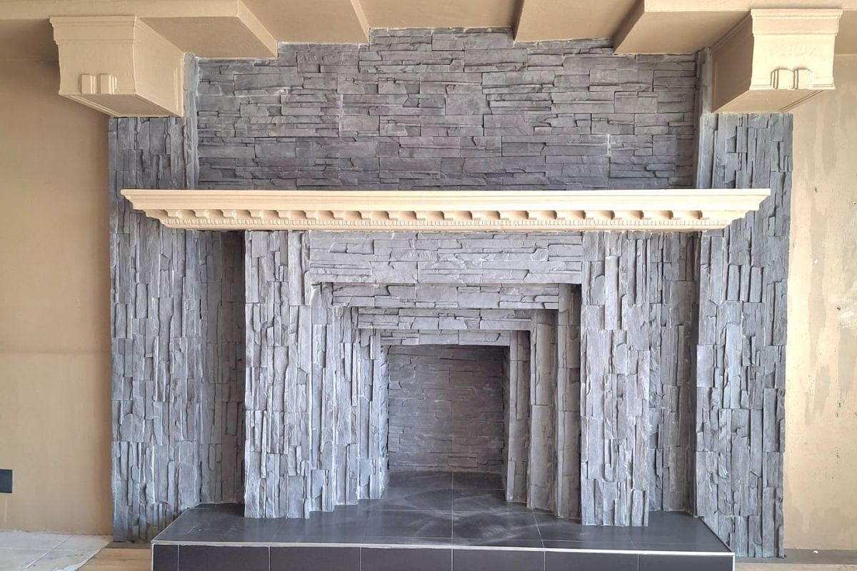 A spacious living area featuring a prominent stone fireplace with a decorative wooden mantelpiece and modern laminate flooring.