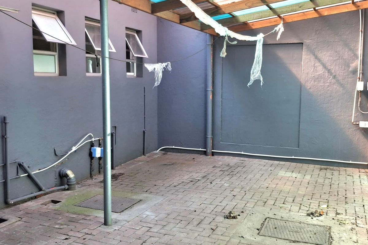 A paved rear courtyard area featuring a timber pergola structure with translucent roofing and external wall-mounted plumbing fixtures.