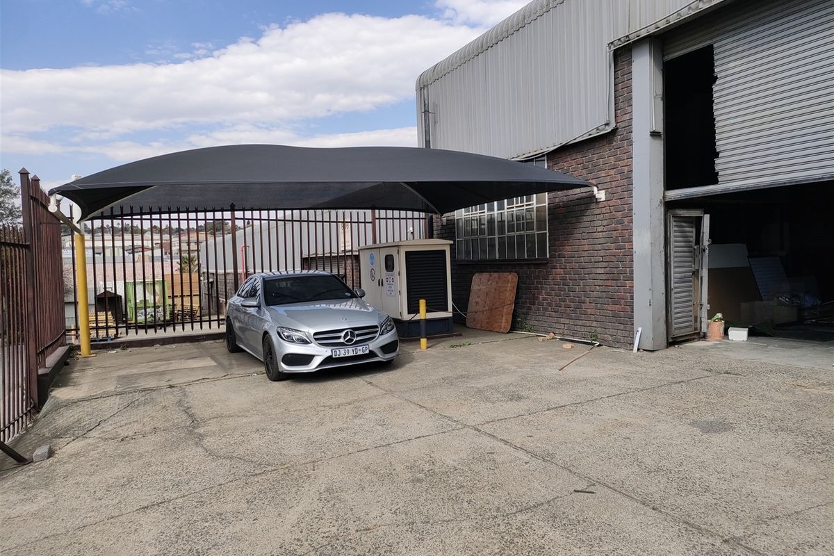 Industrial exterior area featuring a shade sail parking bay, brick and metal facade, and a large roller shutter door access point.