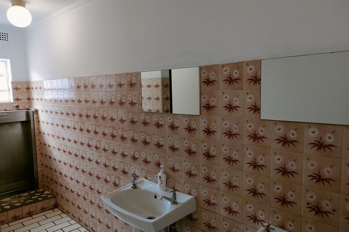 Industrial bathroom facility featuring a pedestal washbasin, wall-mounted urinal, and dated patterned wall tiling.