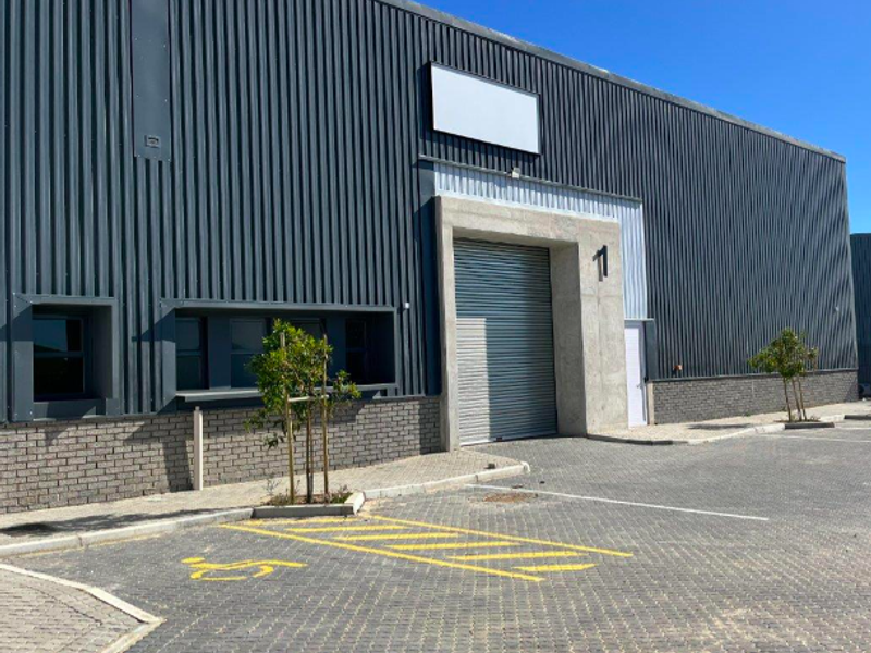 Modern industrial unit featuring dark corrugated metal cladding, a secure roller shutter door, and a paved exterior parking area with an accessible bay.