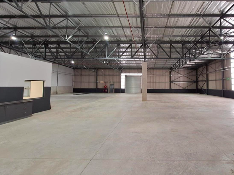 Spacious industrial warehouse featuring high ceilings with exposed steel trusses, polished concrete flooring, and a large roller shutter door for easy access.