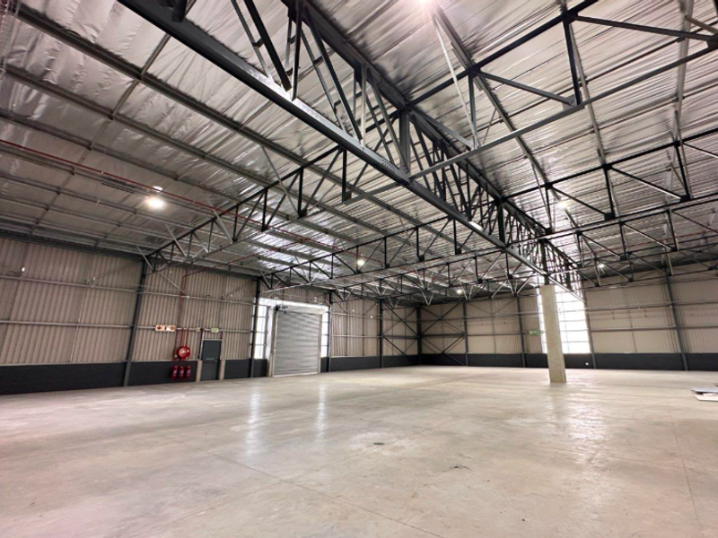 Spacious industrial warehouse featuring high-clearance exposed steel truss roofing, polished concrete flooring, and a large roller shutter door for efficient access.