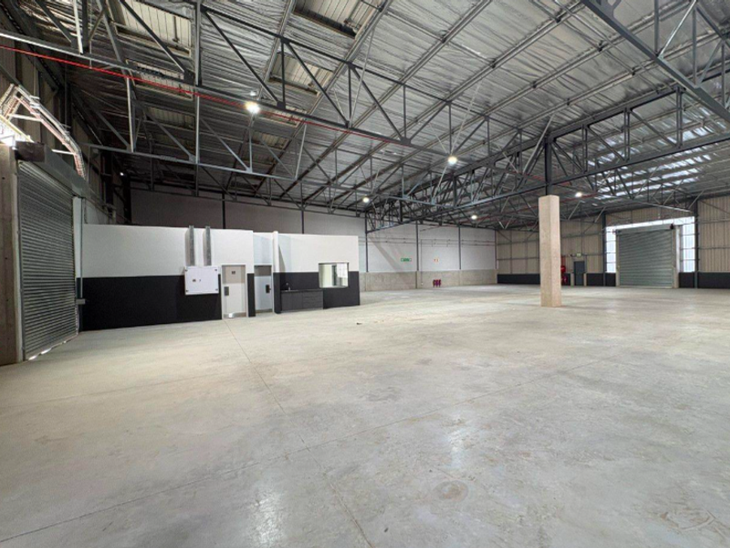 Spacious industrial warehouse featuring high-clearance steel truss roofing, polished concrete floors, multiple roller shutter doors, and an integrated internal office or utility block.