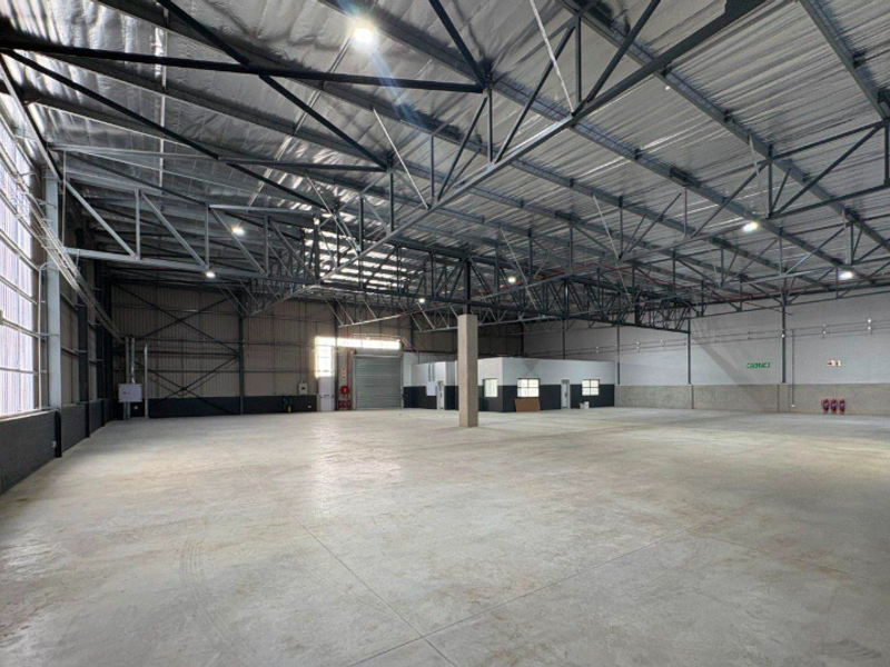 Spacious industrial warehouse featuring high ceilings with exposed steel trusses, polished concrete flooring, and a large roller shutter door for easy access.